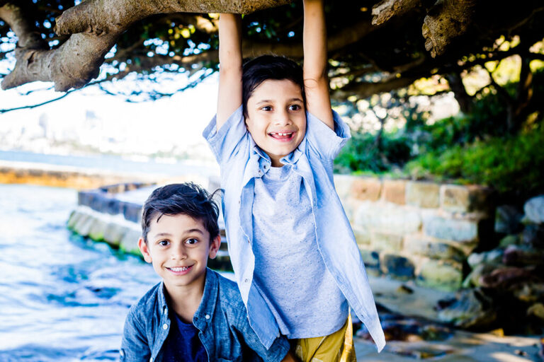 Two boys smiling while one hangs from a tree.