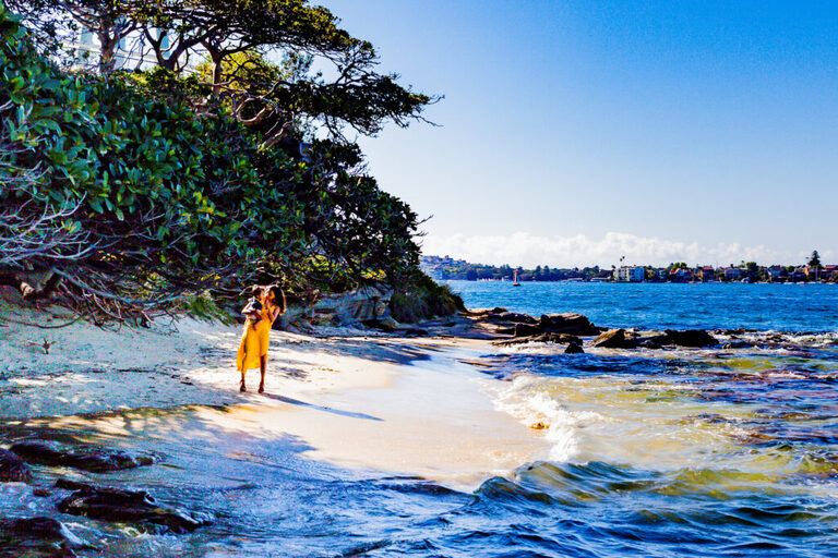A mother and her baby standing ashore of a harbour beach in Sydney