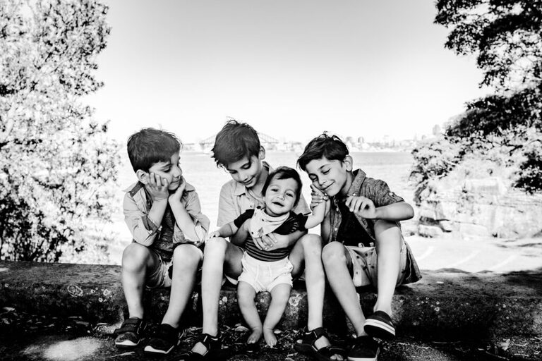 Four boys sitting on a log smiling at the baby in the group